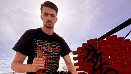 Garreth Conner poses next to a wall of bricks with the word "taxes" on it.