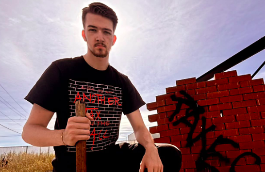 Garreth Conner poses next to a wall of bricks with the word "taxes" on it.